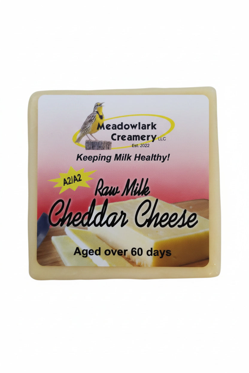 Block of raw milk cheddar cheese with Meadowlark Creamery label on a white background